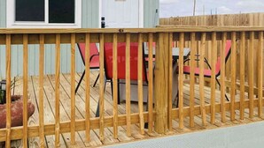 Une terrasse en bois avec une rambarde, une table et des chaises rouges.