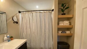 Une salle de bain avec un rideau de douche à rayures, un lavabo avec des articles de toilette, un miroir et des étagères avec des serviettes pliées.