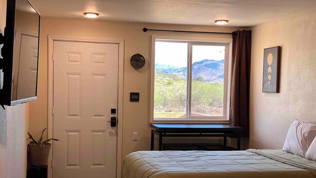 Une chambre à coucher avec un lit, une fenêtre donnant sur les montagnes, une porte et une petite table.