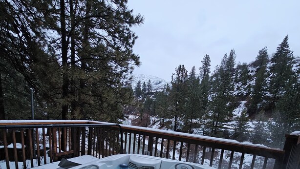 Un bain à remous entouré d’une terrasse en bois, avec de la neige au sol et des arbres en arrière-plan.