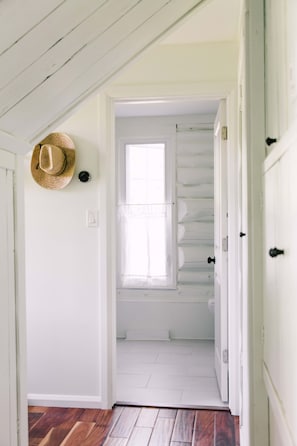 A hallway with a wooden floor, a white door, and a window with a view of a white closet.
