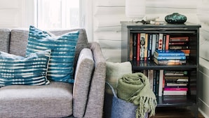 A cozy living room with a grey sofa, a bookshelf, and a window with a view.