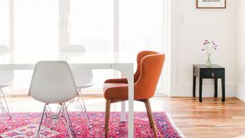 Un salon moderne avec une grande fenêtre, un tapis à motifs, une table blanche et deux chaises.