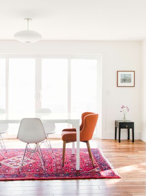 Un salon moderne avec une grande fenêtre, un tapis à motifs, une table blanche et deux chaises.