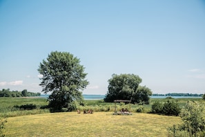 A grassy field with a gazebo and chairs, surrounded by trees and a body of water in the background.