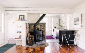 Un intérieur chaleureux avec une cheminée en pierre, un plancher en bois, un coin cuisine avec un bar et un escalier menant à une autre pièce.