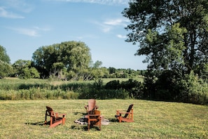 Trois chaises Adirondack en bois, placées dans un champ herbeux, avec des arbres en arrière-plan.