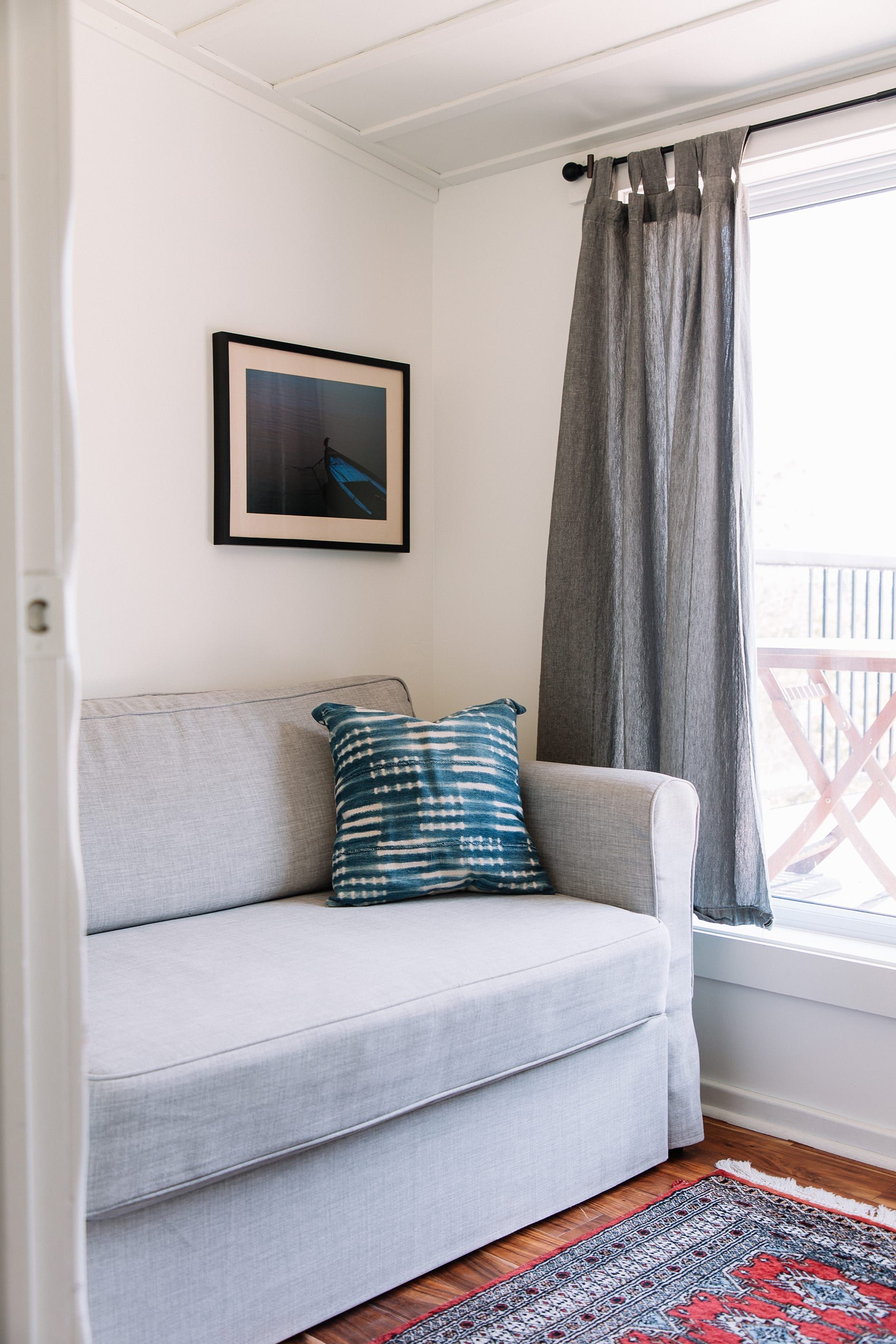 A light grey sofa with a patterned pillow, a framed picture on the wall, and a grey curtain.