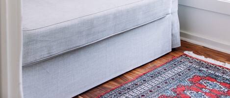 A light grey sofa with a patterned pillow, a framed picture on the wall, and a grey curtain.