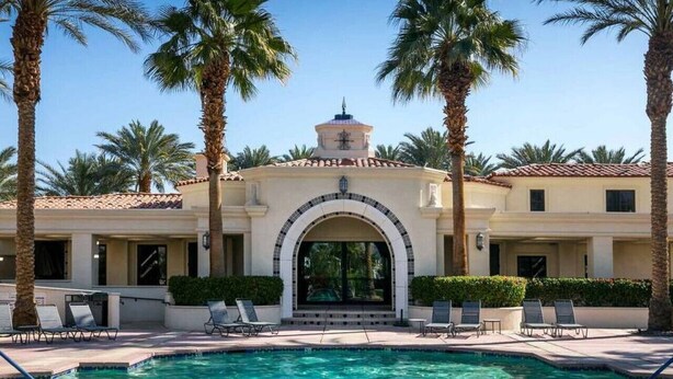 A pool area with a clear blue pool, palm trees, and a building with a tiled archway. - Affordable Desert Getaway w/ Private Pool + Hot Tub! (La Quinta)