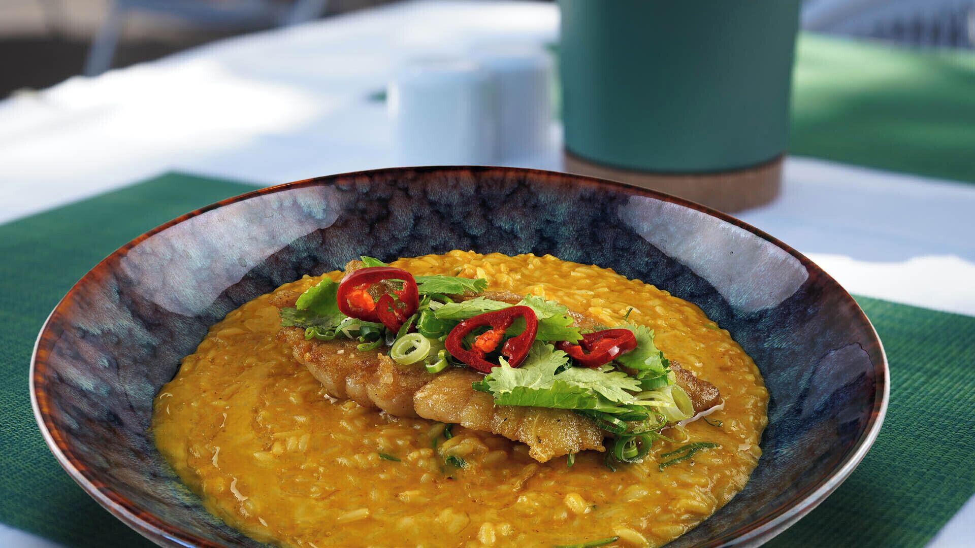 A bowl of soup with a piece of meat and garnishes, placed on a table with a green cloth.