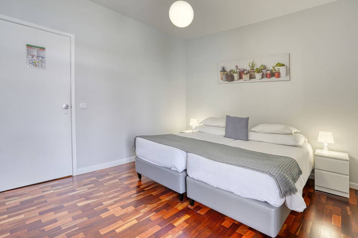 Ein Schlafzimmer mit einem Doppelbett, zwei Nachttischen mit Lampen, einem an der Wand befestigten Pflanzenregal und einer Tür mit Kartenleser.