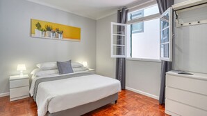 Een slaapkamer met een bed, nachtkastjes, een dressoir, een raam met gordijnen en een schilderij aan de muur.