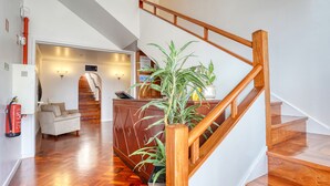 Een modern interieur met een houten trap, een receptiebalie en een zithoek met een bank en een plant in pot.