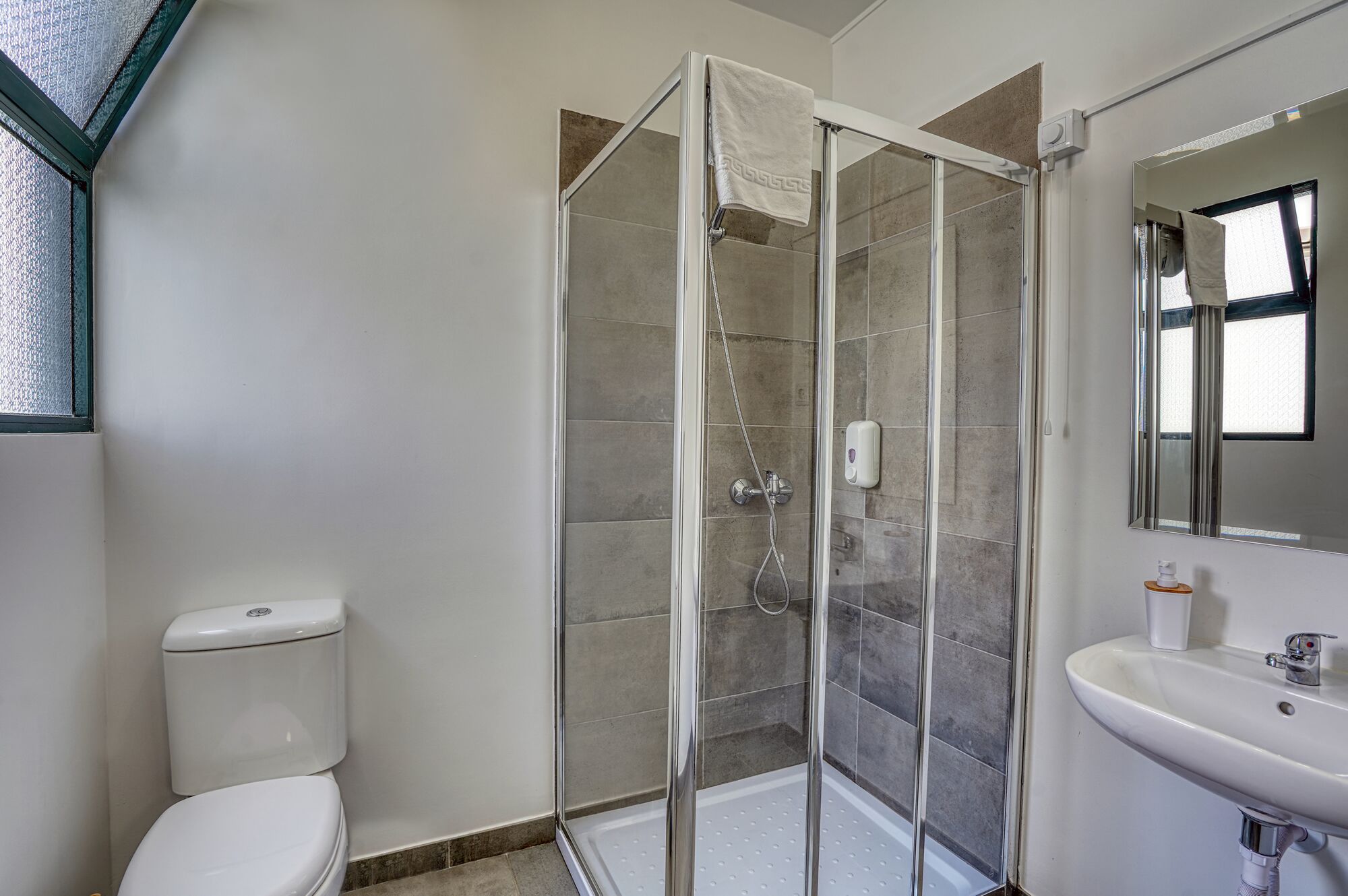 Ein Badezimmer mit Duschkabine, Toilette und Waschbecken mit Spiegel.