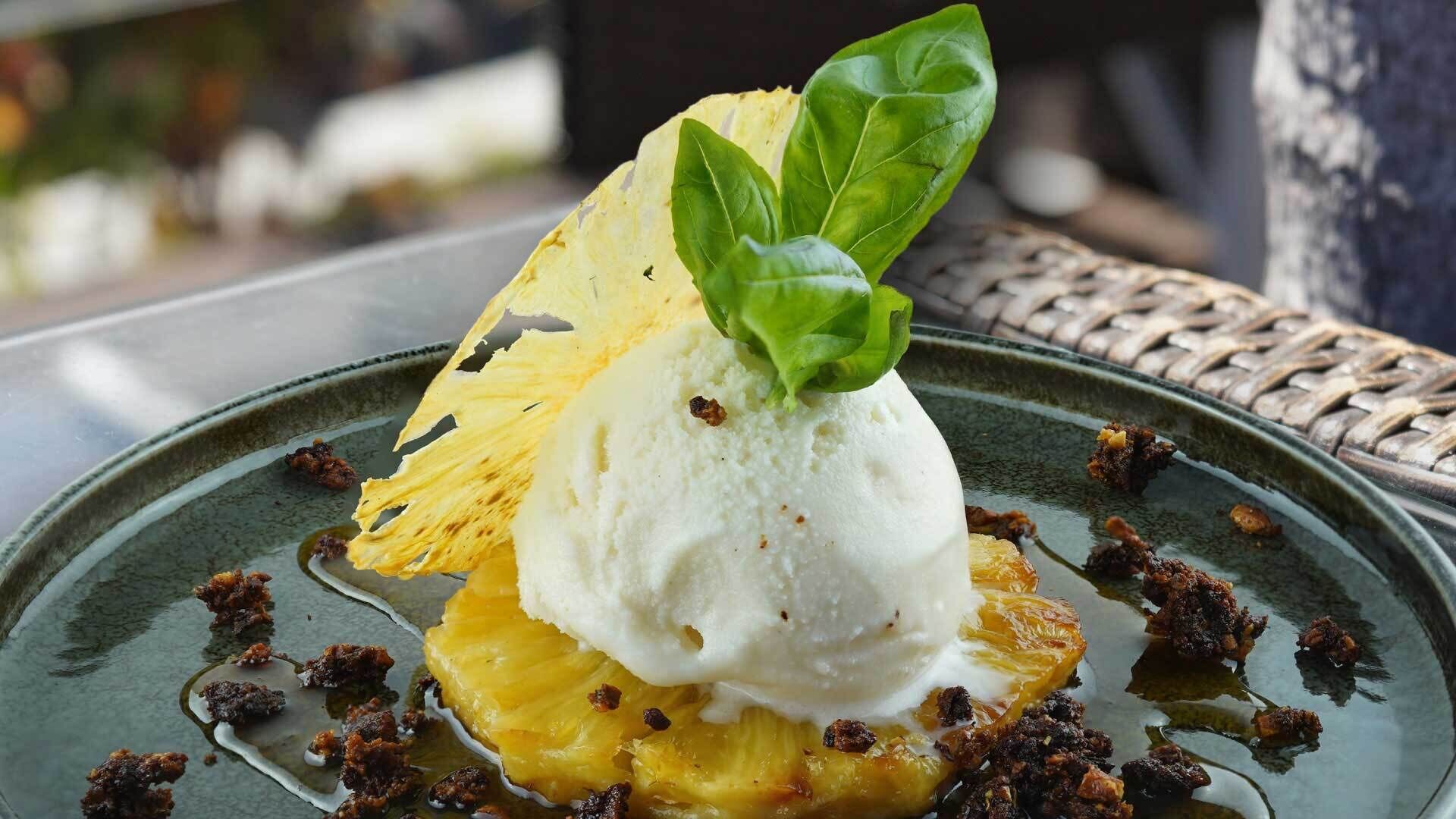 A dessert with a scoop of ice cream on top of a pineapple slice, garnished with a basil leaf.
