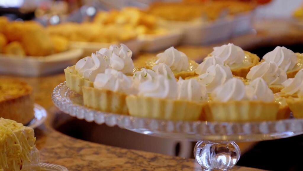 Un présentoir de desserts avec divers gâteaux et pâtisseries, notamment une tarte recouverte de crème fouettée, présentée sur un support en verre.