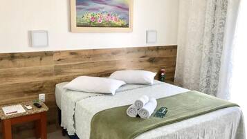 Quarto de hotel com cabeceira de madeira, cama com roupa de cama branca, manta verde e um quadro na parede.