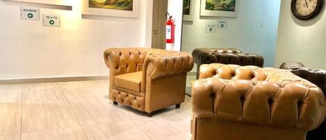 A lobby with beige leather sofas, artwork on the walls, and a clock.