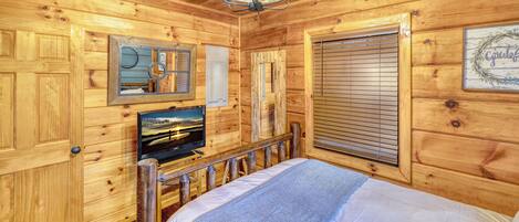 Habitació d'una cabana de fusta amb un llit, una televisió i una finestra amb persianes.