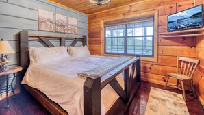 Quarto de cabana de madeira com uma cama, televisão, janela e uma cadeira.