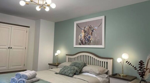 A bedroom with a bed, bedside lamps, a painting, and a wardrobe.