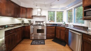 A modern kitchen with dark wood cabinets, stainless steel appliances, and a large window providing natural light. - Wooded & Quiet, but Downtown. Spacious Home w/ Smokeless Fire Pit, Barrel Sauna (Bellaire)