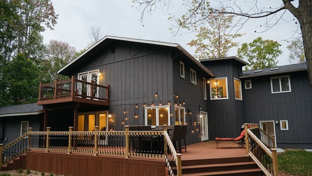 A large, dark-colored house with a wooden deck, a staircase, and a balcony. - Wooded & Quiet, but Downtown. Spacious Home w/ Smokeless Fire Pit, Barrel Sauna (Bellaire)