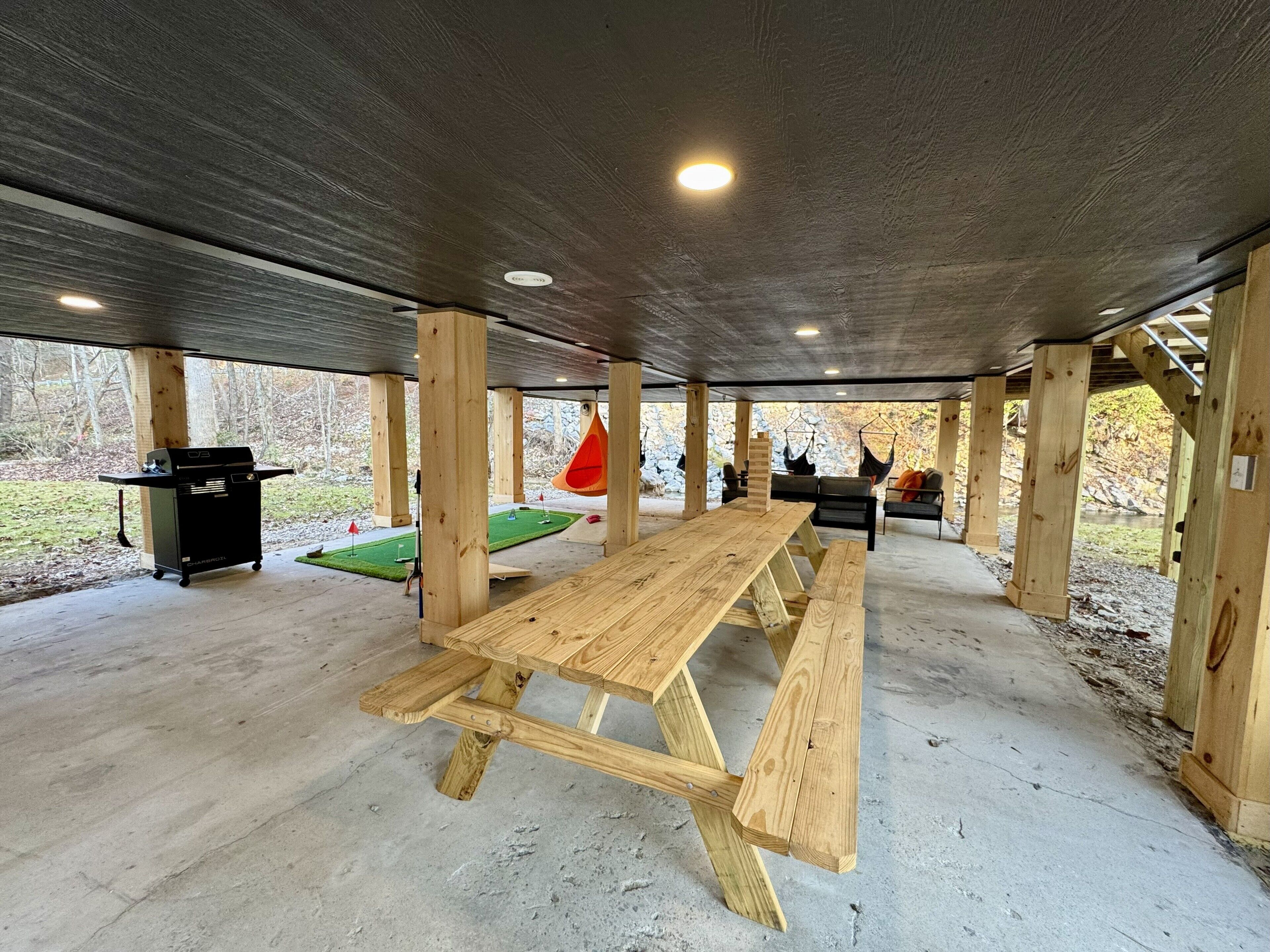 Un espacio al aire libre techado con una mesa de picnic, asientos y una parrilla.