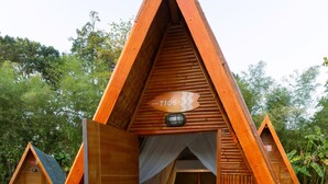 Una cabaña de madera triangular con una cama, una silla y una mesita.
