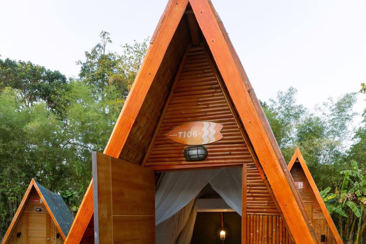 A triangular wooden cabin with a bed, a chair, and a small table.
