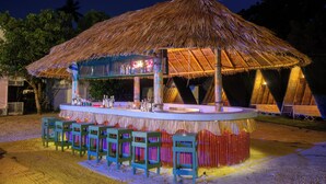 Zona de bar con techo de paja, una barra y taburetes.