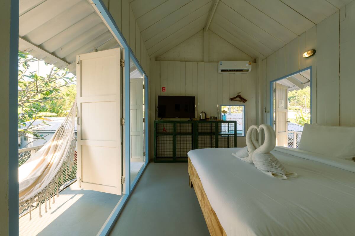 A room with a bed, a TV, a hammock, and a view of the outside.