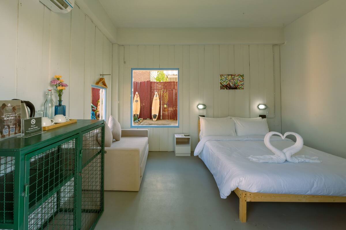 A bedroom with a bed, a desk, a chair, a window, and a view of the outside.