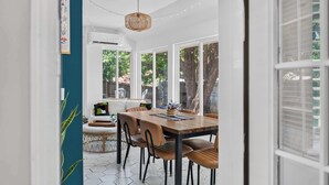A dining area with a wooden table and chairs, large windows, and a hanging light fixture.
