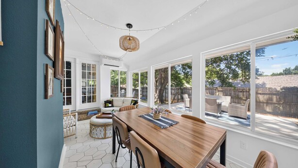 A dining area with a wooden table and chairs, large windows, and a hanging light fixture.
