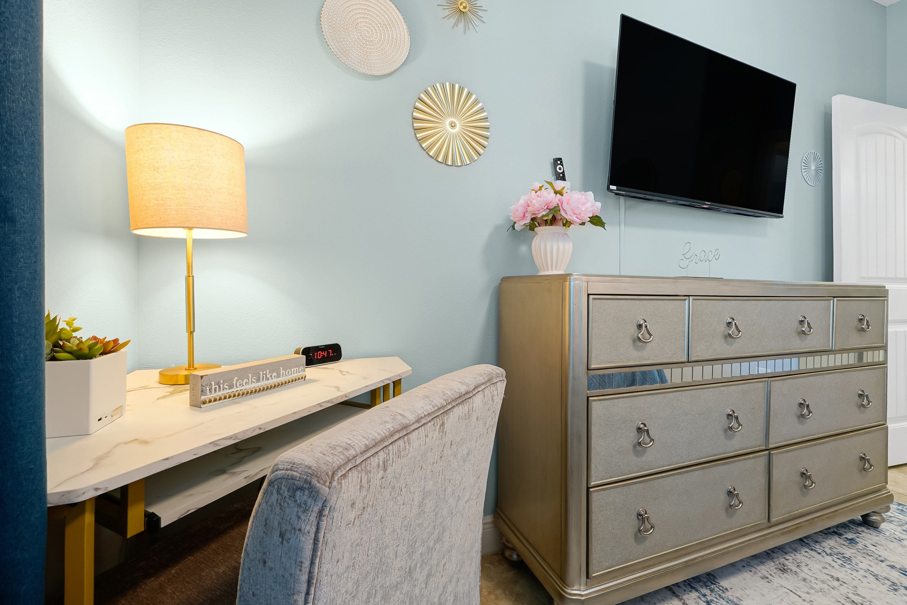 A room with a desk, a lamp, a dresser, a TV, and a wall clock.