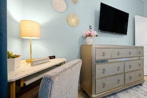 Une pièce comprenant un bureau, une lampe, une commode, un téléviseur et une horloge murale.