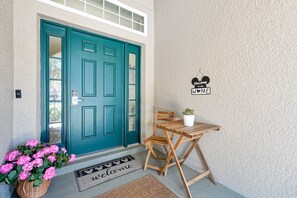 A teal door with a window, a wooden bench, a potted plant, and a welcome mat. - 5-bedroom pool home with spa and Mario game room at Solterra Resort, near Disney (Davenport)
