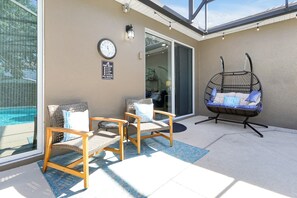 Un espace aménagé au bord de la piscine, comprenant deux fauteuils en osier, un fauteuil suspendu, une horloge et un panneau indiquant les règles de la piscine.