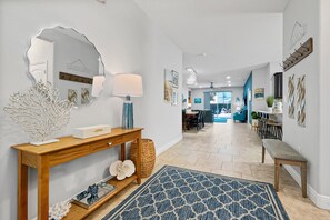 Un couloir avec une console en bois, un miroir, une lampe et un tapis à motifs bleus.