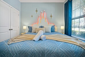 Een slaapkamer met een bed, kussens, een deken, een kunstwerk aan de muur en een raam met gordijnen.