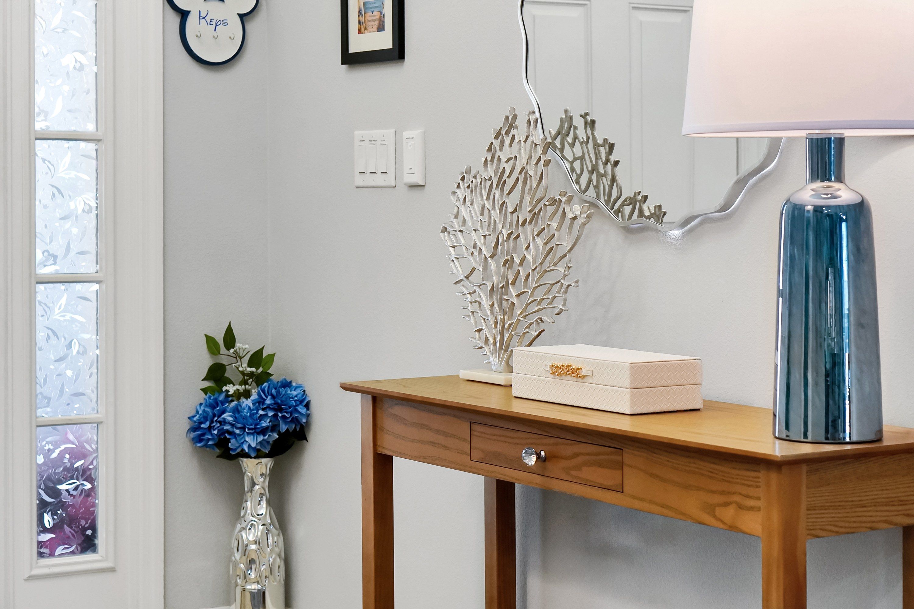 A wooden desk with a lamp, a vase with flowers, and a decorative branch.