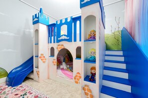 Een kinderspeelplaats met een speelhuisje in kasteelthema, inclusief een glijbaan en een trap.