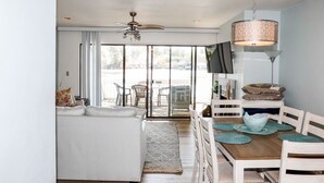 A modern living room with a white sofa, a dining table with chairs, a ceiling fan, and a large window with a view of the outdoors. - Bethany Beach Sea Colony Resort Condo w/Lake Views.   (Bethany Beach)