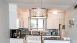 A modern kitchen with white cabinets, a central island, and a hanging light fixture. - Bethany Beach Sea Colony Resort Condo w/Lake Views.   (Bethany Beach)
