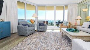 Ein geräumiges Wohnzimmer mit einem großen Schiebeglastür, die auf einen Balkon führt, zwei gemusterte Sessel, ein Sofa, ein Couchtisch und ein blaues Schränkchen.