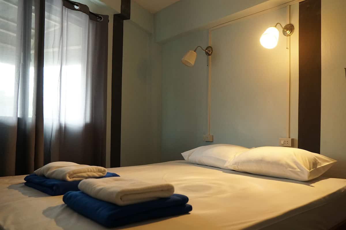 Een hotelkamer met een bed, twee bedlampen, een raam met gordijnen en een stopcontact.
