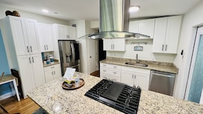 A kitchen with white cabinets, a stainless steel refrigerator, a built-in stove, and a granite countertop.
