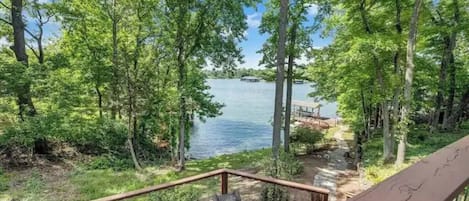 Relax on the deck overlooking the serene lake, surrounded by lush greenery and tall trees, with a bench and table for a peaceful retreat.